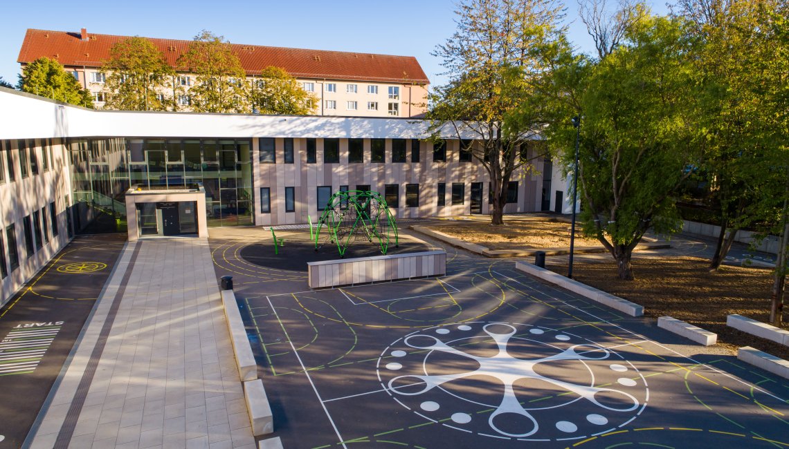 Der Hansehort von au&szlig;en. Der Au&szlig;enbereich mit freien Spielfl&auml;chen und B&auml;umen ist zu sehen.
