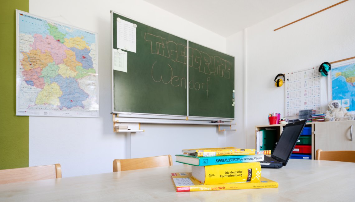 Im Lernraum liegen Lehrb&uuml;cher auf dem Tisch und an der Tafel steht Tagesgruppe Wendorf